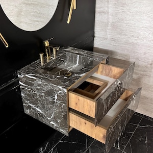 May include: A black marble bathroom vanity with two wooden drawers. The drawers are open, revealing the interior. The vanity has a black marble countertop with a white sink.