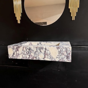 A calacatta viola marble sink with brown and purple veins. The sink is rectangular and has a square basin. The sink is sitting on a white surface.