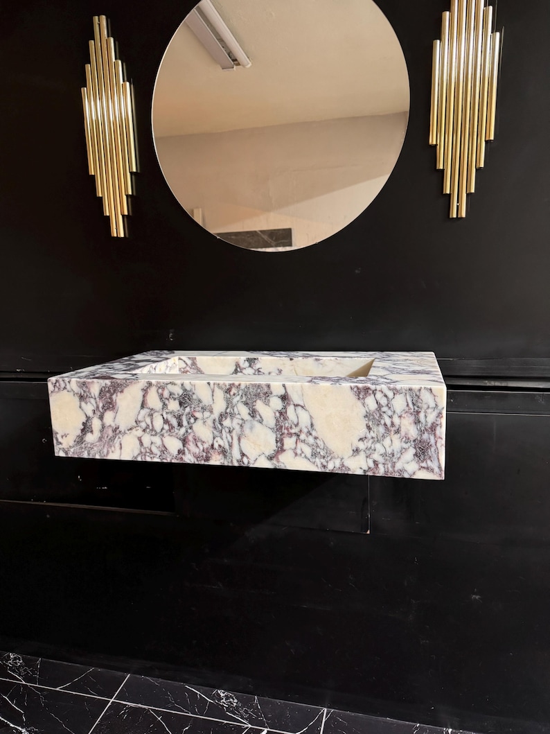 A calacatta viola marble sink with brown and purple veins. The sink is rectangular and has a square basin. The sink is sitting on a white surface.