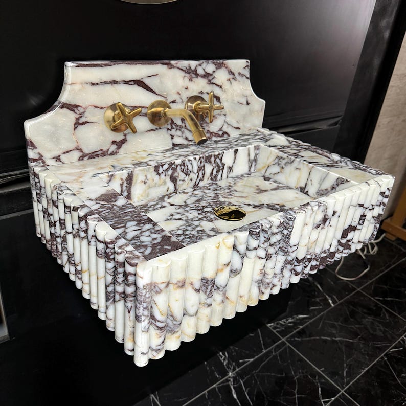 A calacatta viola marble sink with brown and purple veins. The sink is rectangular and has a square basin. The sink is sitting on a white surface.