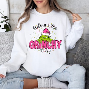 May include: White sweatshirt with a pink and green graphic of the Grinch with the text "feeling extra Grinchy today".