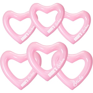 May include: Six pink heart-shaped inflatable photo booth props with the text "Bride's Babes" printed on five of them and "Bride" printed on one.