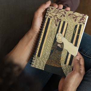 May include: A spiral bound notebook with a beige cover featuring an illustration of a woman in a black and gold dress standing in a doorway. The woman has long white hair and is holding a small object in her hands. The background is a brick wall with a window and a crescent moon.