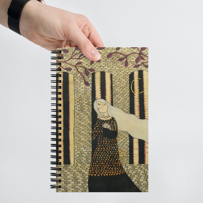 May include: A spiral bound notebook with a colorful illustration of a woman in a black dress with a geometric pattern. The woman has long white hair and is standing in front of a stone wall with a crescent moon in the background.