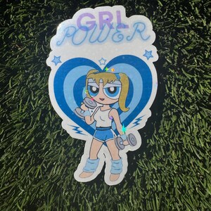 May include: A blue and white sticker with a cartoon character lifting weights. The character has blonde hair and blue eyes. The sticker says "GRL POWER" in a glittery font.