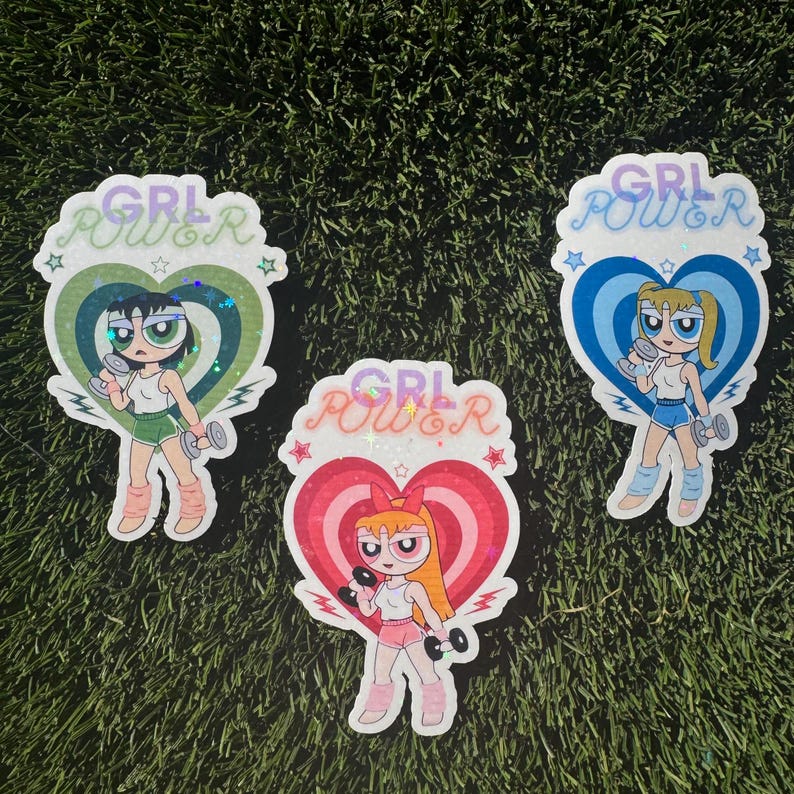 May include: Three colorful stickers featuring cartoon girls with the text "GRL POWER" in a glittery font. Each sticker has a different color heart shape and a different cartoon girl.