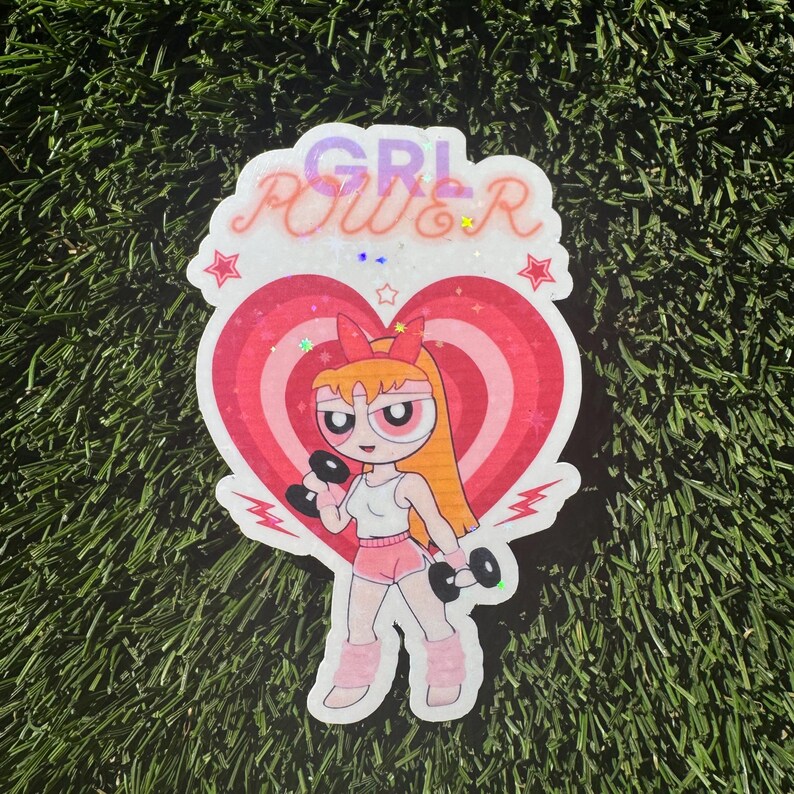 May include: A pink and red glitter sticker with a cartoon character lifting weights. The character has orange hair and is wearing a white tank top, pink shorts, and pink leg warmers. The sticker says "GRL POWER" in pink and purple glitter letters.
