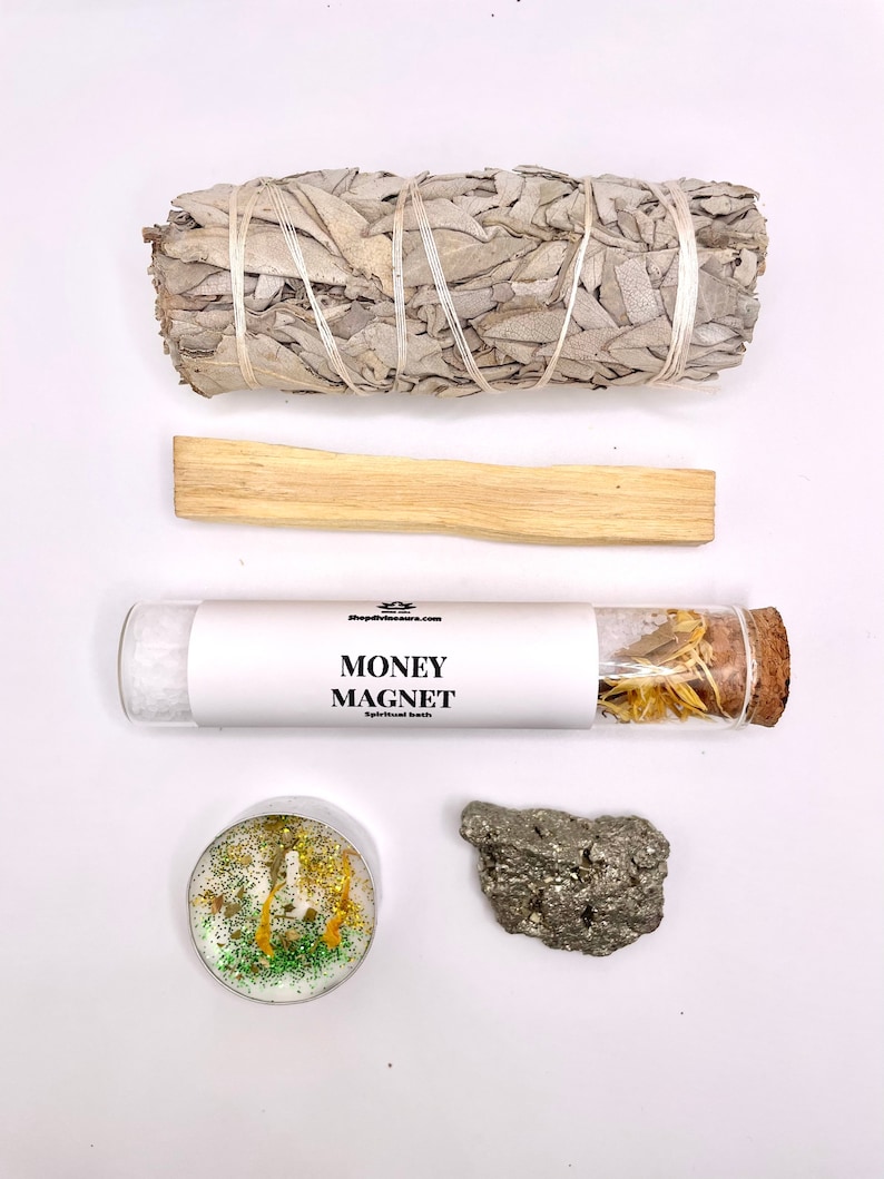 May include: A white sage smudge stick, a palo santo stick, a glass vial with dried herbs labeled "MONEY MAGNET Spiritual Bath", a green and gold glitter candle, and a piece of pyrite.