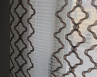 Può includere: Tende bianche e trasparenti con un motivo geometrico marrone. Il motivo è una forma di diamante ripetuta con una linea ondulata su ogni lato.