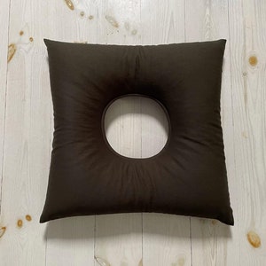 May include: A dark brown donut pillow with a large hole in the centre. The pillow is made of a soft, plush fabric and is ideal for supporting the neck and head.