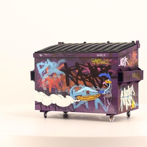 May include: A miniature purple dumpster with graffiti art and a cartoon Road Runner character. The dumpster has a black lid and small wheels. The graffiti includes various colors and text.