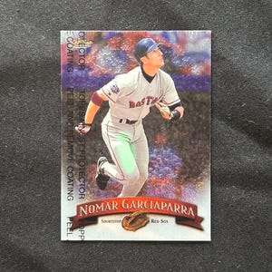 Op de afbeelding: Een honkbalkaart met Nomar Garciaparra, een shortstop voor de Red Sox. De kaart heeft een holografische achtergrond en een rood-wit-blauw kleurenschema.