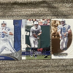 Può includere: Tre carte da collezione con Peyton Manning, un ex quarterback della NFL. Le carte sono della stagione 2003 e mostrano Manning con la sua uniforme degli Indianapolis Colts. Le carte sono in buone condizioni e hanno uno sfondo bianco con accenti blu e argento.