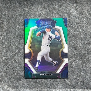 May include: A baseball card featuring Don Sutton, a former Major League Baseball pitcher. The card is from the Select series and features a holographic design with a green, blue, and purple colour scheme. The card shows Sutton in a pitching motion, wearing a Los Angeles Dodgers uniform.