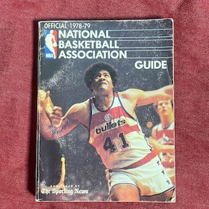 Puede incluir: Una guía de la Asociación Nacional de Baloncesto de 1978-79. La portada presenta a un jugador de baloncesto con un uniforme rojo, blanco y azul con la palabra "bullets" y el número "41". Publicado por The Sporting News.
