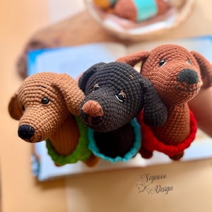 May include: Three crocheted dachshund dog toys in shades of brown and black, each with a different colored collar: green, blue, and red. The toys have black eyes and noses. The toys are handmade.