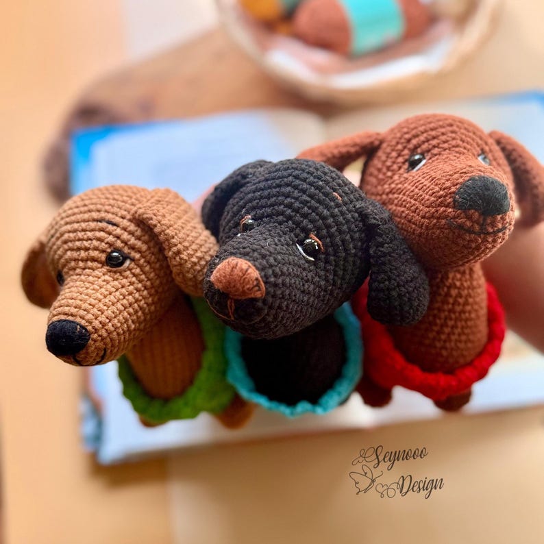May include: Three crocheted dachshund dog toys in shades of brown and black, each with a different colored collar: green, blue, and red. The toys have black eyes and noses. The toys are handmade.