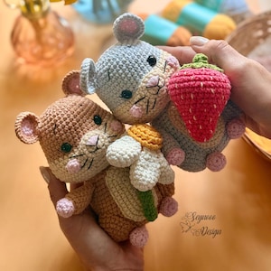 Puede incluir: Juguetes de ganchillo hechos a mano: un ratón, una fresa y una margarita. Los ratones son de color marrón y gris con detalles en rosa. La fresa es roja con la parte superior verde. La margarita es blanca con el centro amarillo.