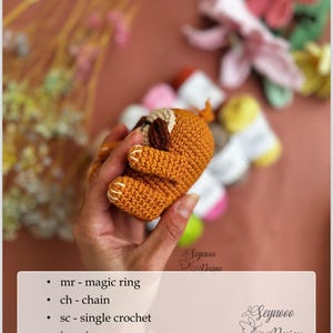 Puede incluir: Primer plano de un juguete de amigurumi de perezoso tejido a crochet en colores marr&oacute;n y naranja. El juguete est&aacute; siendo sostenido por una mano. La imagen incluye el texto "Seynoo Design" y "Abbreviations" con una lista de abreviaturas de crochet.