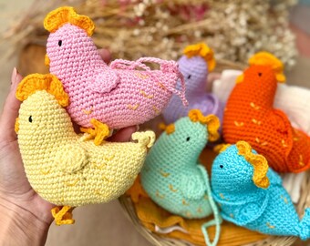 May include: A collection of colorful, crocheted chicken figurines in various shades of pink, yellow, orange, blue, green, and purple. Each chicken has a yellow comb and feet, with a small black eye. The chickens are arranged in a woven basket.