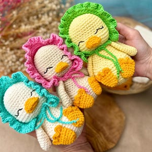 Puede incluir: Tres patitos hechos a mano con ganchillo en amarillo, blanco y naranja. Cada patito tiene un gorro de diferente color: verde, rosa y azul. Los patitos tienen los ojos cerrados y picos naranjas. El trabajo de ganchillo es detallado y el efecto general es encantador.