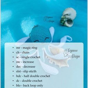 Pu&ograve; includere: Un giocattolo amigurumi in crochet blu con un viso sorridente e ali in crochet bianco. Il giocattolo &egrave; seduto su una superficie blu con due conchiglie bianche. L'immagine include un elenco di abbreviazioni di crochet, tra cui mr, ch, sc, inc, dec, slst, hdc, dc, blo, flo e st. Il testo "Seynooo Design" appare due volte nell'immagine.