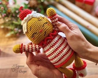 May include: A handmade crochet gingerbread man doll. The doll has a yellow head and body, with a red and white striped outfit. It has a red hat and white trim. The doll is being held by a person.