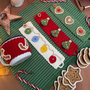 May include: A red and white crocheted mug cozy and three crocheted mug wraps in red, white, and green. The wraps are decorated with crocheted Christmas tree and heart designs. Also included are star-shaped coasters and a candy cane.
