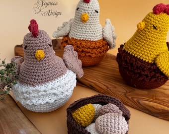 May include: Three crocheted chickens, one brown, one white with an orange bottom, and one yellow with a brown bottom. A brown crocheted basket with five crocheted eggs, two brown and three yellow, sits in front of the chickens.