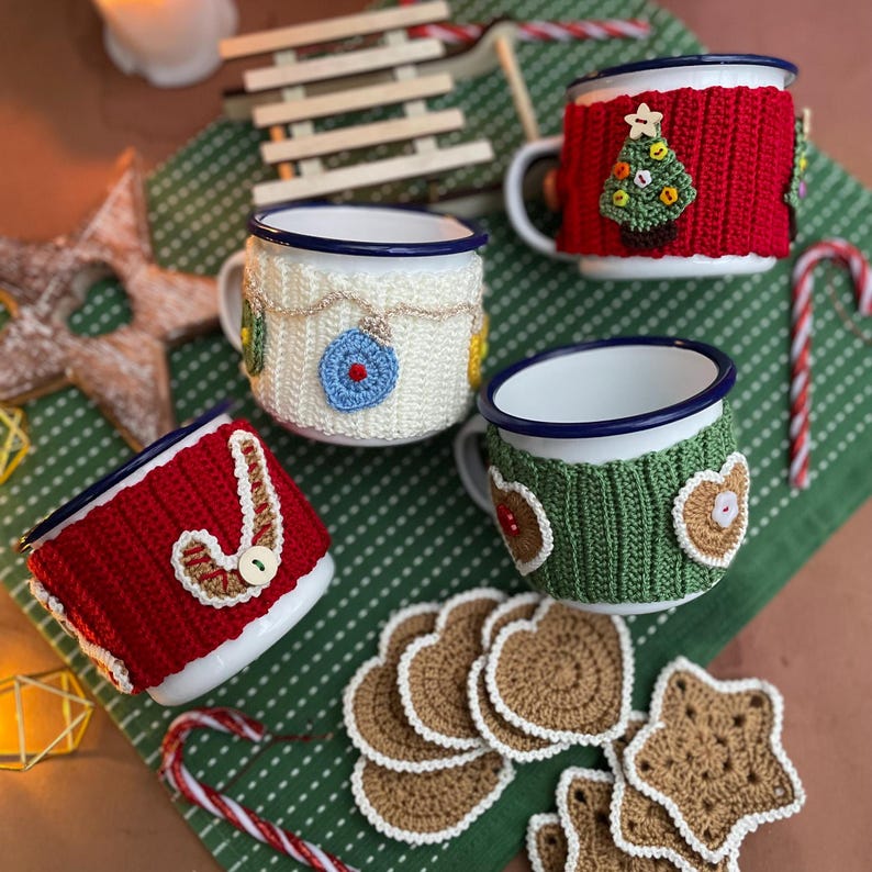 May include: Four white enamel mugs with blue rims, each adorned with a unique, colorful, crocheted cozy. The cozies feature Christmas-themed designs like a tree, candy cane, and ornaments. Crochet coasters and candy canes complete the festive scene.
