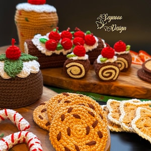 Puede incluir: Una colección de alimentos de crochet con temática navideña, que incluyen un tronco de Navidad, un pudín de Navidad y galletas. Los artículos están dispuestos sobre una superficie de madera con un fondo verde.