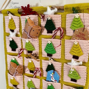 Puede incluir: Un calendario de adviento navideño hecho a mano con un diseño de ganchillo. El calendario presenta pequeños bolsillos con árboles de Navidad de ganchillo, bastones de caramelo y pequeñas cajas de regalo. El fondo es de color rosa claro con un borde amarillo.