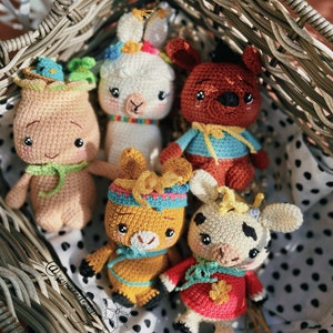 May include: A collection of six handmade crochet dolls in a wicker basket. The dolls include a tree-like figure with a bird, a white llama, a brown bear, a yellow llama, and a cow. Each doll has unique features and colorful accents.