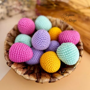 May include: A wicker basket filled with crocheted Easter eggs in various colors, including pink, purple, yellow, and green.