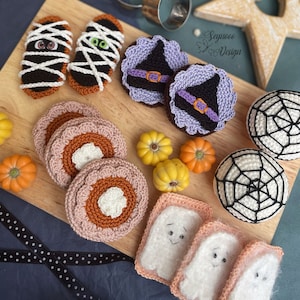 May include: A collection of crocheted Halloween-themed decorations, including ghosts, pumpkins, witches, and spiders. The decorations are displayed on a wooden cutting board with a black and white polka dot ribbon.