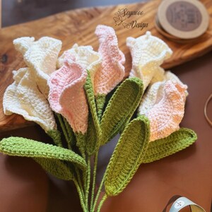 May include: A bouquet of crocheted calla lilies in white and pink with green leaves. The flowers are arranged in a cluster and have a realistic appearance.