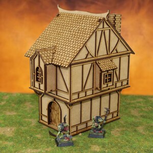 May include: A wooden model of a two-story house with a gabled roof and a chimney. The house is painted in a light brown color and has a door and windows. Two small green figures are standing in front of the house.