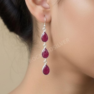 Può includere: Orecchini pendenti in argento con tre pietre preziose rosse a forma di goccia. Gli orecchini sono sospesi a un gancio e presentano una finitura lucida. Le pietre preziose sono incastonate in una lunetta d'argento.