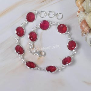 May include: A silver bracelet with oval, deep red gemstones. The bracelet has a delicate chain design and a lobster clasp. The gemstones are evenly spaced along the chain, creating a classic and elegant look. The bracelet is approximately 18 cm in length.