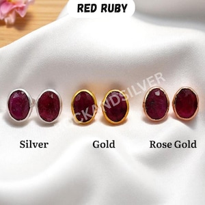 May include: Three pairs of oval-shaped red ruby stud earrings in silver, gold, and rose gold settings. The earrings are displayed on a white satin surface. The text "Red Ruby" is at the top, and "Silver", "Gold", and "Rose Gold" are below the earrings.