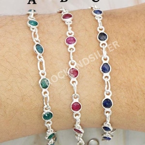 Può includere: Tre braccialetti in argento con pietre preziose. Il braccialetto A presenta pietre verdi, il braccialetto B pietre rosse e il braccialetto C pietre blu. Ogni braccialetto è collegato da una delicata catena.