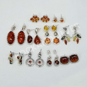 May include: A selection of silver earrings with amber gemstones in various shapes. Designs include studs, drops, and dangles, with amber hues from light honey to dark red. The earrings are presented on a white background.