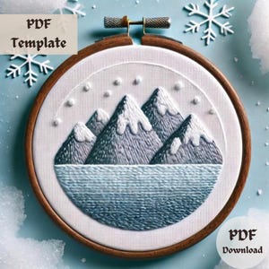 Puede incluir: Una plantilla PDF para bordado que presenta una cordillera nevada con un lago en primer plano. El diseño está en un aro con un marco de madera.