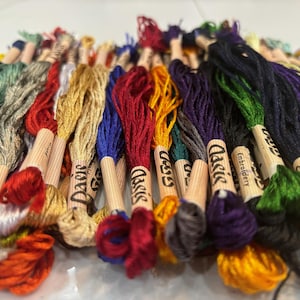May include: A collection of embroidery floss spools in various colors, including red, blue, green, yellow, and brown. The spools are labeled "Classic Embroidery" and "Daisy".