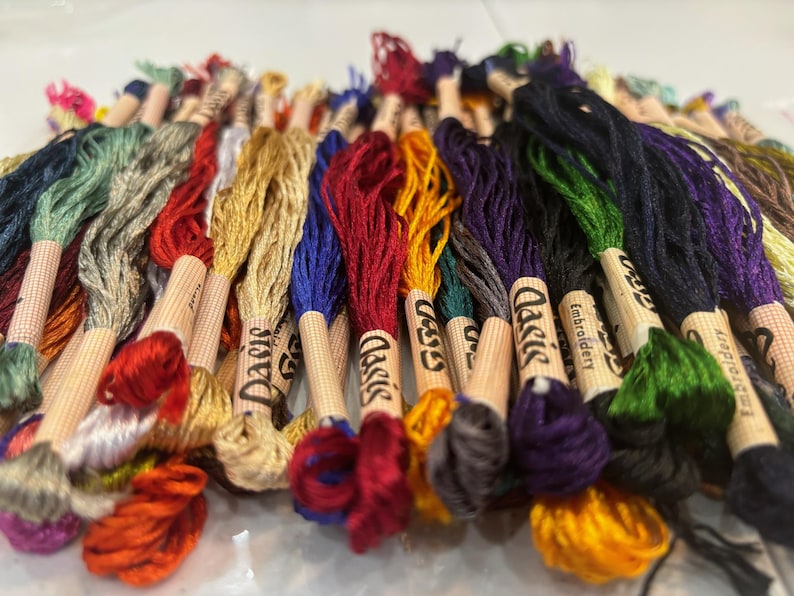Puede incluir: Una colecci&oacute;n de carretes de hilo de bordar en varios colores, incluyendo rojo, azul, verde, amarillo y marr&oacute;n. Los carretes est&aacute;n etiquetados como "Classic Embroidery" y "Daisy".
