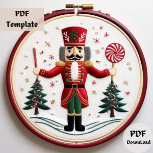 May include: Embroidered nutcracker with a red and green uniform, holding a candy cane and a lollipop. The nutcracker is surrounded by two small Christmas trees and snowflakes on a white background. The image includes the text "PDF Template" and "PDF Download".