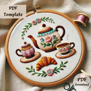May include: Embroidered tea set design in a wooden hoop. The design includes a teapot, teacup, teacup with saucer, croissant, and floral accents. The text "PDF Template" and "PDF Download" are visible.