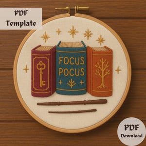 Op de afbeelding: Een borduurring met drie kleurrijke boeken, waarvan één met de tekst "FOCUS POCUS". Een sleutel en een boom sieren de andere boeken. Twee toverstokken staan eronder. De tekst "PDF Template" en "PDF Download" zijn ook aanwezig.