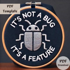May include: A black embroidery hoop with white embroidery that reads "It's not a bug it's a feature" with a stylized white bug in the center.