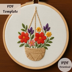 May include: A PDF template for embroidery featuring a hanging basket with orange, yellow, and purple flowers. The basket is made of brown yarn and is hanging from a white string.